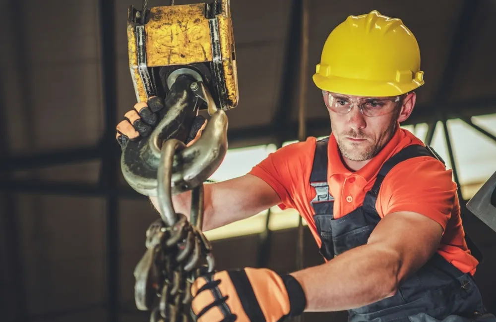 Operator ridicând o sarcină cu lanțuri într-o hală industrială